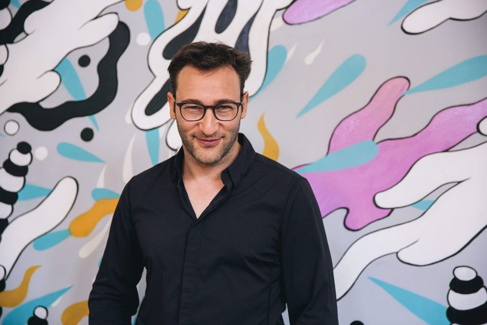 A photograph of Simon Sinek in front of a colorful wall