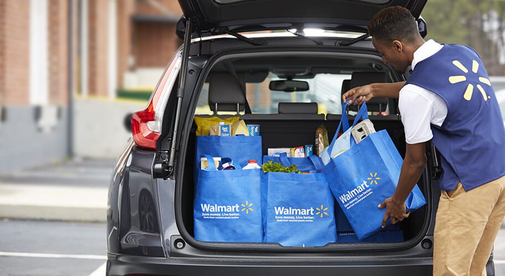 A Walmart worker filling a car with grocery delivery items.