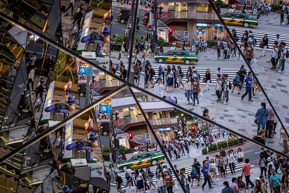 People are seen reflected in a shopping mall mirror at a busy intersection in the shopping district of Harajuku on June 18, 2015 in Tokyo, Japan