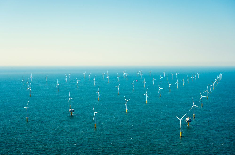 An aerial photo of a few dozen offshore wind turbines in the ocean.