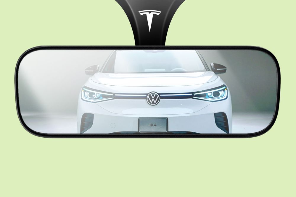 An illustration of a rearview mirror with a Tesla logo up top; reflected in the mirror is an approaching white Volkswagen ID.4 SUV