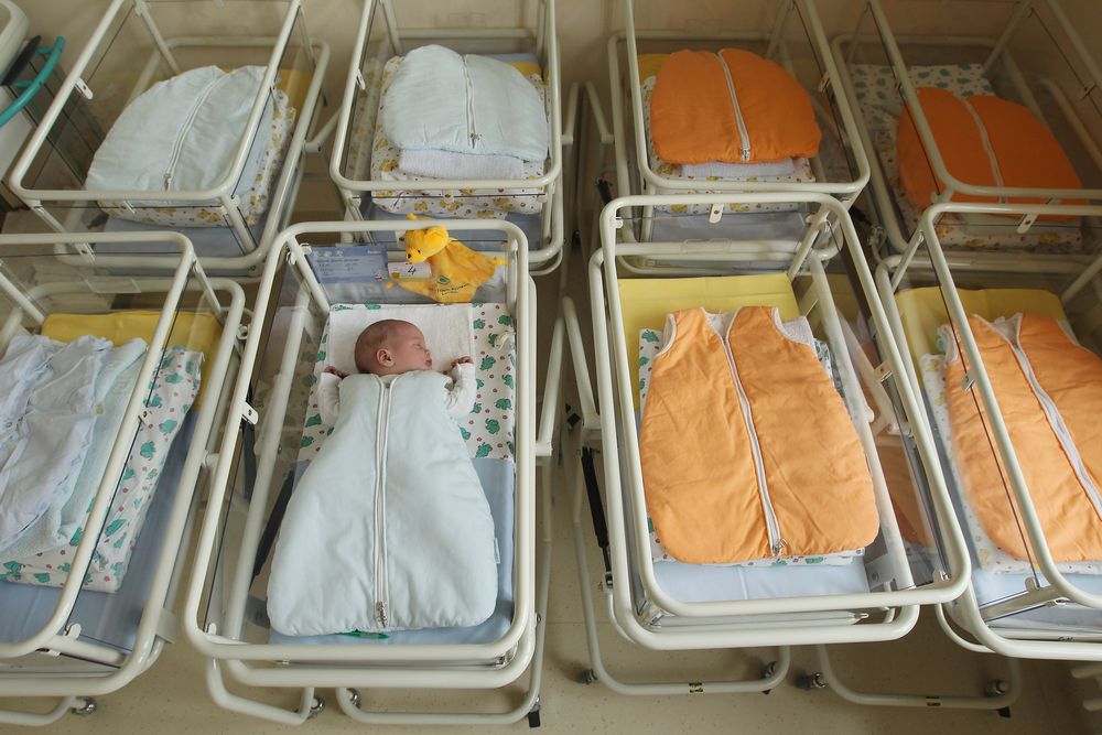 Newborn baby in hospital bed surrounded by empty hospital beds