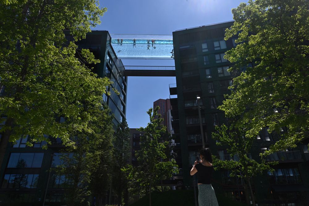 A photograph of London's Sky Pool, a completely see-through pool suspended like a bridge between the tops of two buildings. A handful of people are seen from below swimming in it on a sunny afternoon.