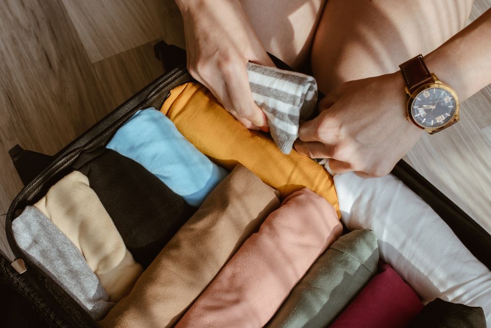 Close up of tourist woman open suitcase roll and pack colorful cloths for traveling