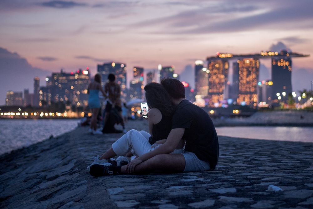 A couple sit on a breakwater with a view of the city skyline in the Mari...