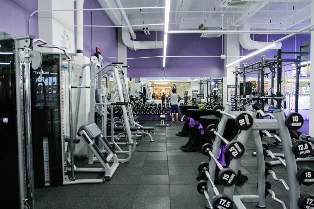 Empty gym besides one man lifting weights in front of a mirror