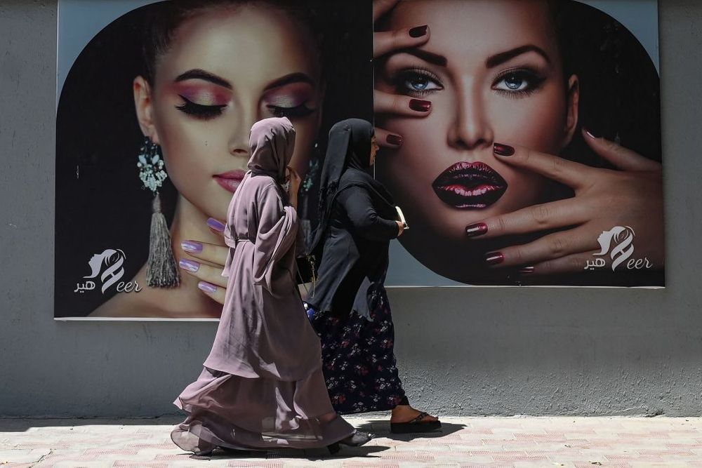 Burqa clad women walk past a billboard put up on the wall of a beauty salon in Kabul