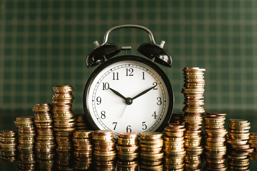 A classic analog alarm clock is surrounded by stacks of coins