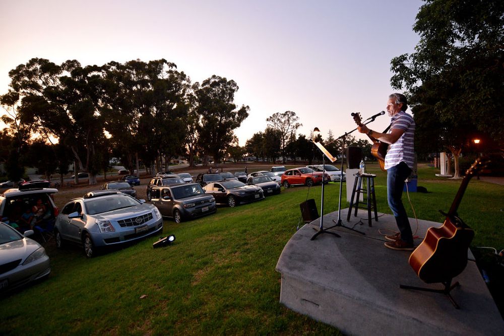 Man playing guitar on stage with people watching in their cars