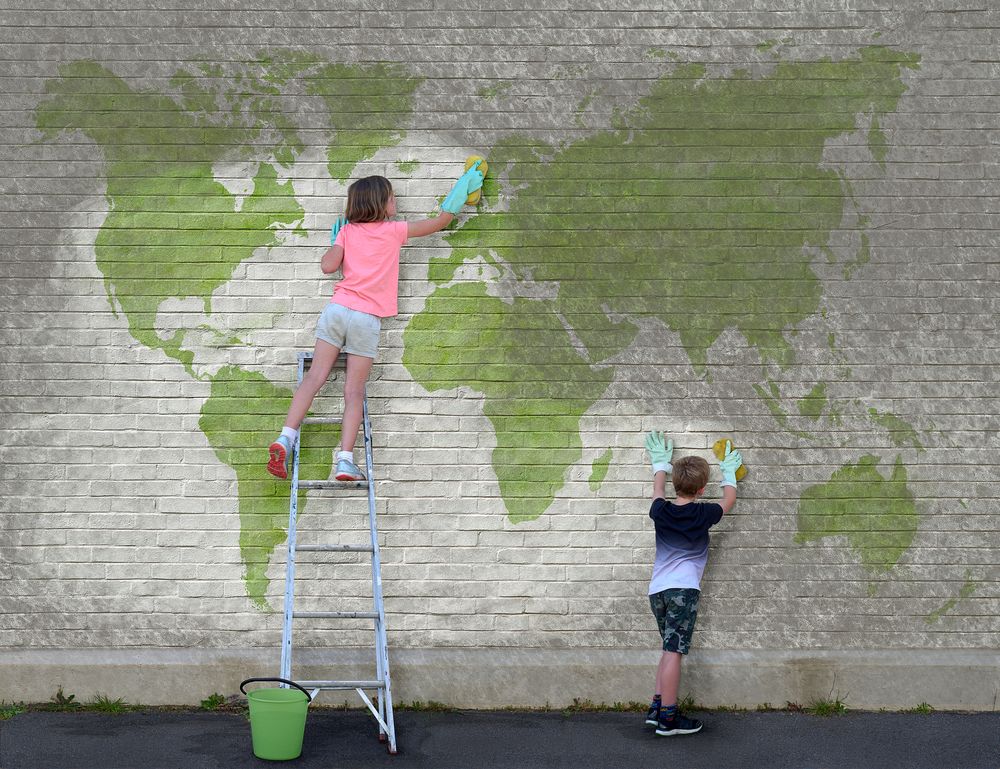 A young girl and a young boy cleaning dirt off a world map mural. She is standing on a ladder and he is standing on the ground. South Africa, August 2019.