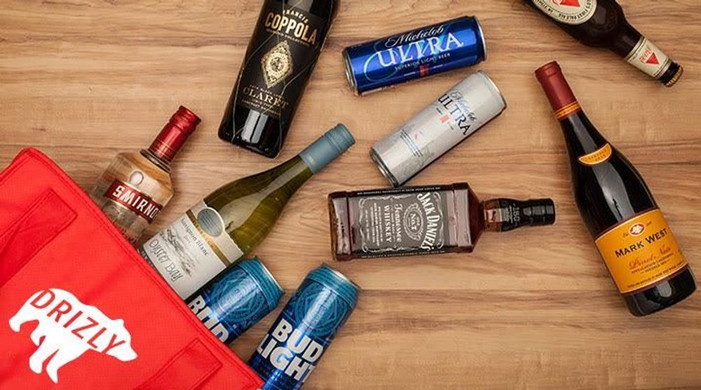 A photograph of a red bag with the Drizly logo (a white bear with the word "Drizly" in it" on a wooden table; spilling out of the bar are various bottles of wine, beer, and liquor